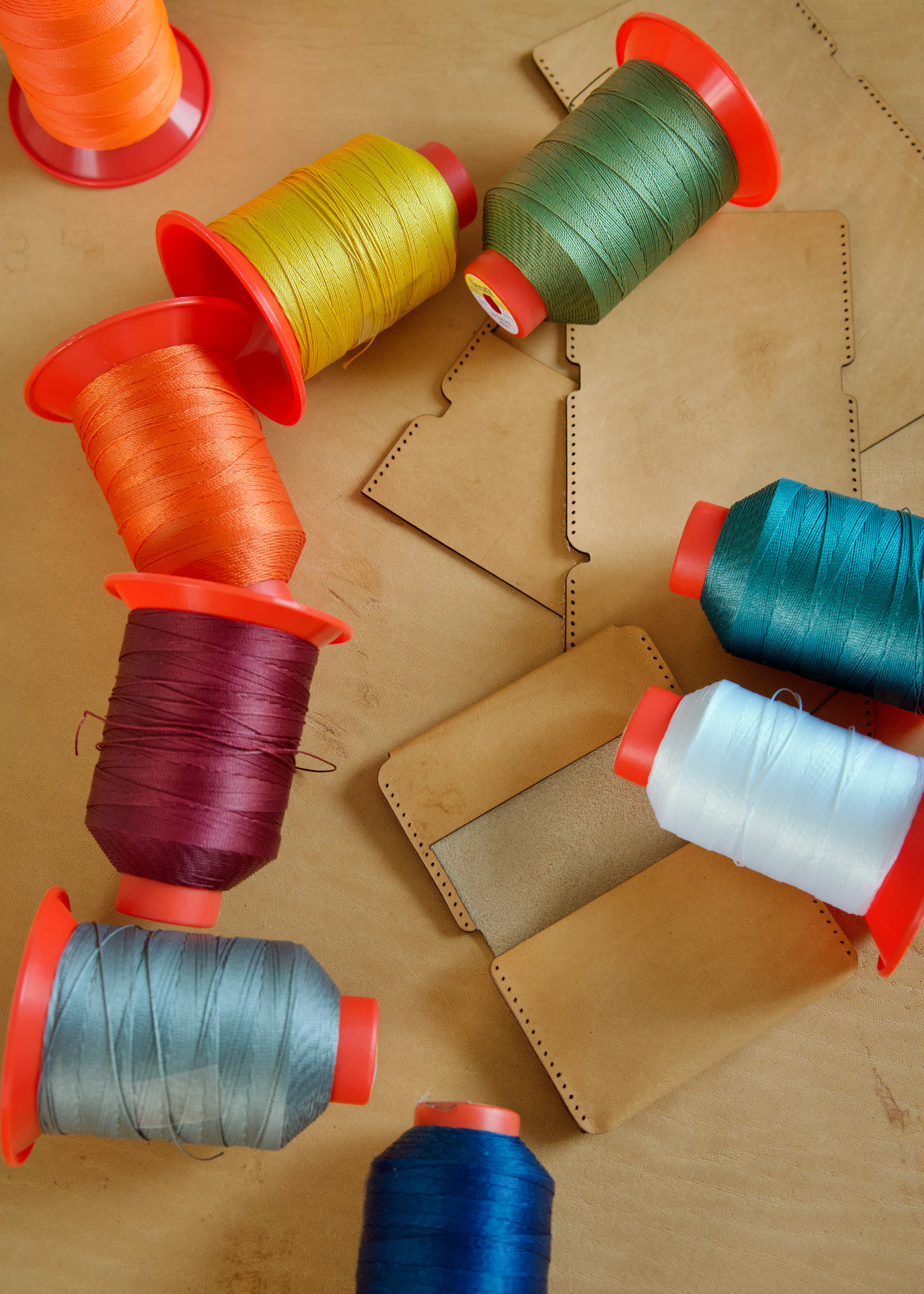 The raw parts used to build the wallets surrounded by spools of colorful thread used for the stitching